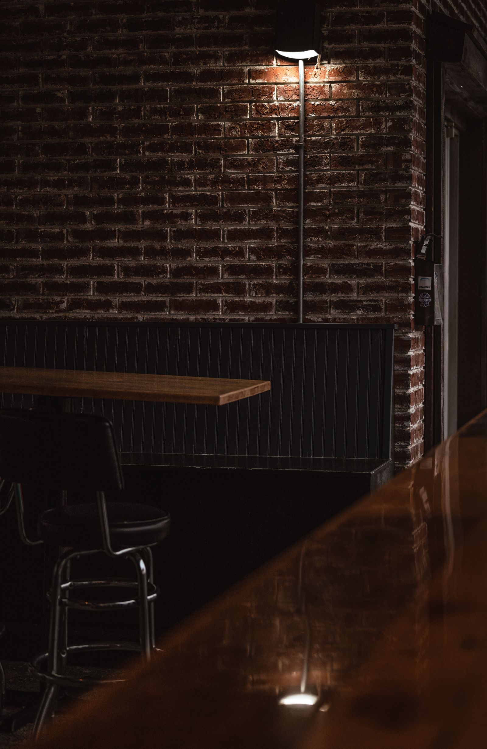 Photo d’illustration — salle de restaurant sombre, brique apparente, lumière chaude rasante, tables en bois