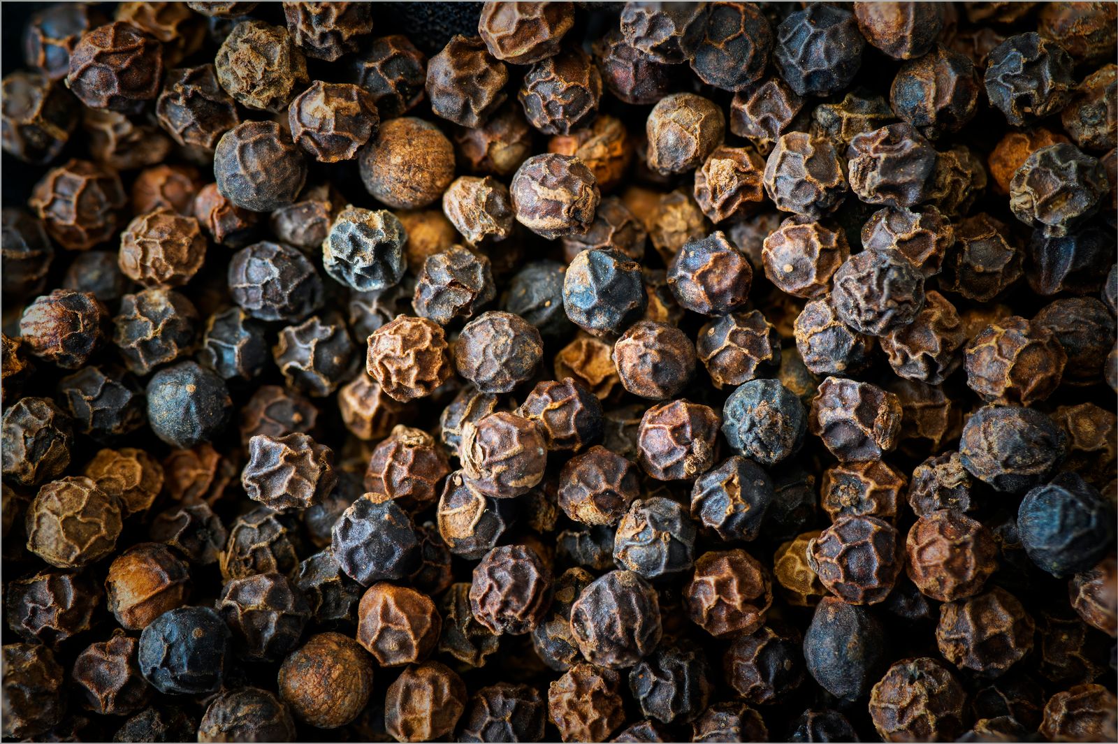 Photo d’illustration — grains de poivre noir en gros plan très serré, fond sombre, texture